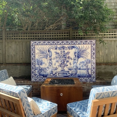 Conjunto de cadeiras de madeira com estofos azuis e brancos e painel decorativo azul e branco num espaço exterior