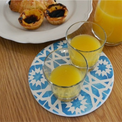 Dois copos com sumo laranja e jarro sobre prato decorado azul e branco com croissants e pastéis de nata num prato branco