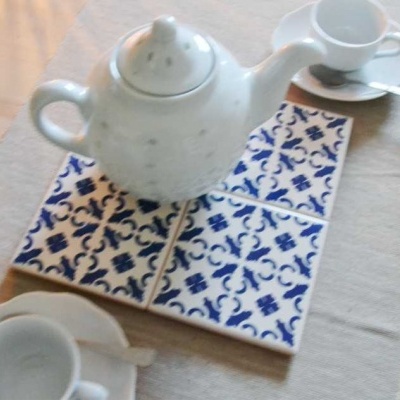 Conjunto de chá com bule, chávenas e suporte de azulejos azul e branco numa mesa de madeira