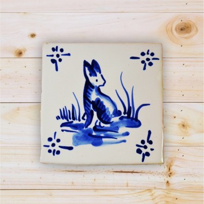 Azulejo quadrado branco com pintura azul de animal e flores sobre madeira clara
