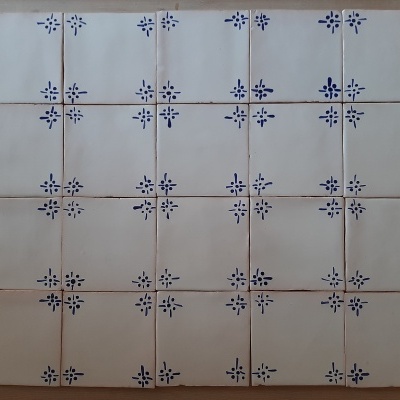 Azulejos quadrados bege com padrão azul em cruz dispostos sobre superfície de madeira