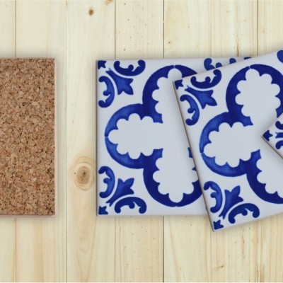 Quatro azulejos quadrados, um em cortiça castanha e três com padrão azul e branco floral sobre madeira clara.