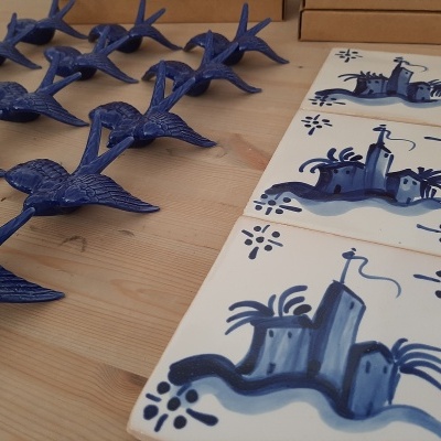 Azulejos brancos com padrão azul de castelo e suportes para velas azuis em forma de pássaros sobre mesa de madeira