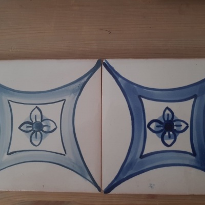 Dois azulejos azuis e brancos com padrão geométrico e floral sobre madeira.