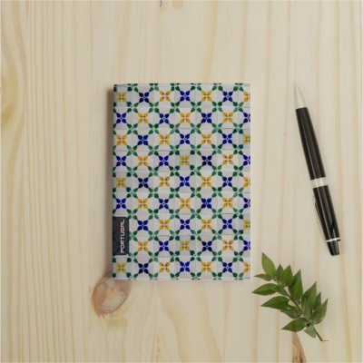 Caderno com capa decorada, caneta preta e planta sobre mesa de madeira clara