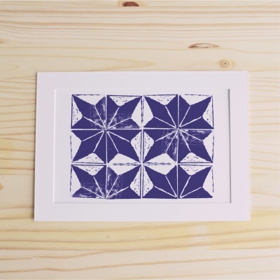 Gravura azul com padrão geométrico em moldura branca sobre madeira clara