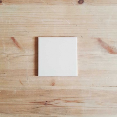 Azulejo branco quadrado sobre mesa de madeira clara