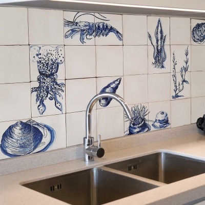 Azulejos brancos com desenhos azuis de mariscos e animais marinhos atrás de pia dupla em inox e torneira prateada