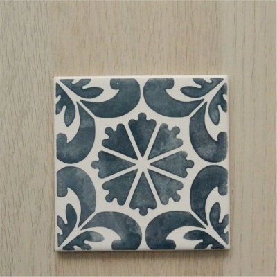 Azulejo quadrado com padrão decorativo azul e branco sobre superfície de madeira