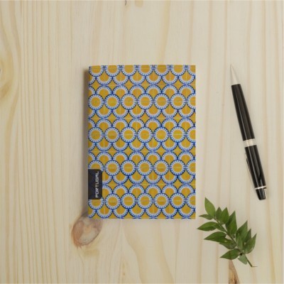 Caderno com capa amarela e azul, caneta preta e folha verde sobre mesa de madeira