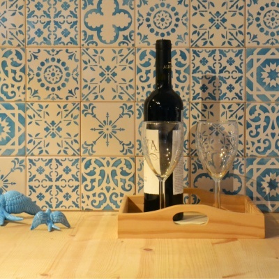 Garrafa de vinho e copos de cristal numa bandeja de madeira sobre mesa com azulejos azuis e brancos ao fundo