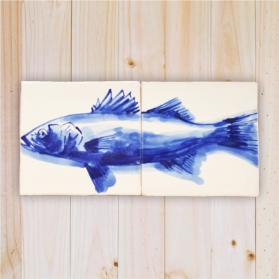Dois azulejos brancos com desenho azul de um peixe sobre madeira clara