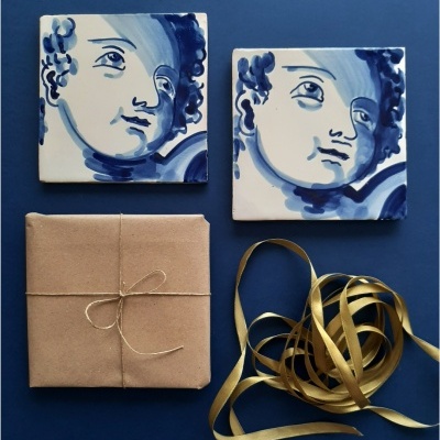 Dois azulejos decorativos com rostos azuis, embrulho castanho e fita dourada sobre superfície azul