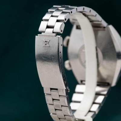 Relógio de pulso com bracelete metálica prateada e fecho com símbolo