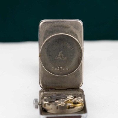 Relógio mecânico aberto mostrando interior metálico com número e texto