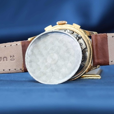 Relógio de pulso dourado com pulseira de couro castanho e mecanismo interno visível