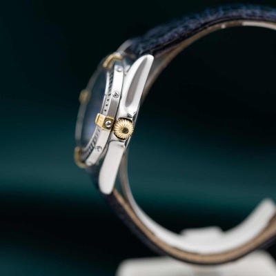 Relógio de pulso em visão lateral com pulseira preta de pele e coroa dourada