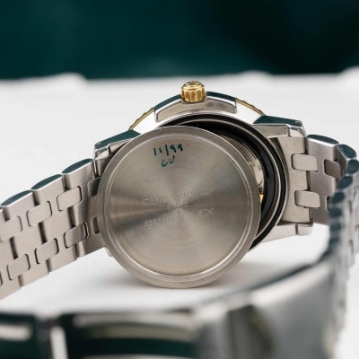 Relógio metálico com tampa traseira aberta e inscrições visíveis