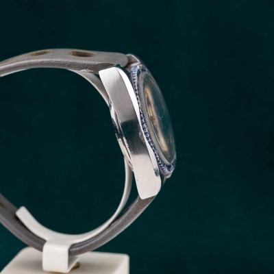 Relógio vintage com caixa metálica, bezel azul e bracelete de couro cinza