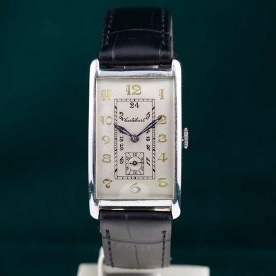 Relógio de pulso retangular com bracelete preta e mostrador branco com números dourados