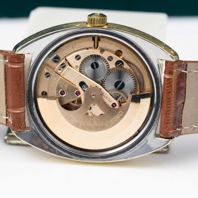 Relógio mecânico com caixa metálica, mecanismo interno dourado visível e pulseira de couro castanha