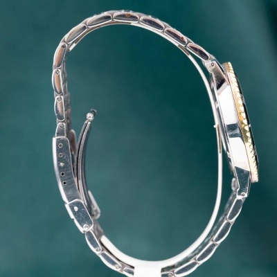 Relógio de pulso com bracelete metálica prateada e aro dourado visto de lado