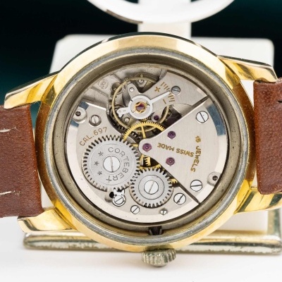 Relógio com caixa dourada e correia castanha, mecanismo interno visível