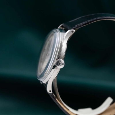 Relógio de pulso prateado com bracelete em pele castanha sobre fundo verde.