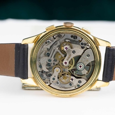 Relógio de pulso dourado com mecanismo exposto e pulseira de couro castanha