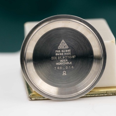 Peça metálica redonda com inscrições Omega e detalhes de fabricação