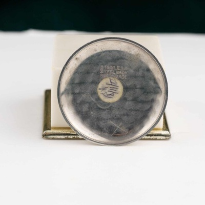 Mostrador redondo em metal e vidro com suporte branco e dourado.