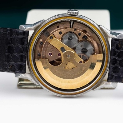 Relógio com mecanismo visível em metal dourado e correia preta