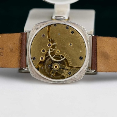 Relógio de pulso aberto mostrando mecanismos internos dourados com pulseira castanha em couro