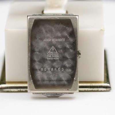 Relógio retangular com bracelete branca sobre suporte branco e base metálica