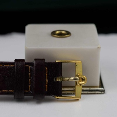 Correia de relógio em couro castanho escuro com fivela dourada sobre base branca