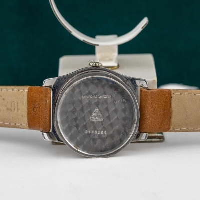 Relógio com caixa metálica e bracelete de couro castanho sobre suporte branco