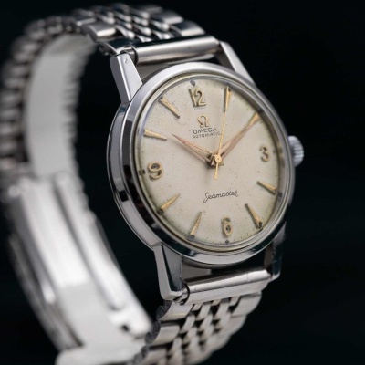 Relógio Omega Seamaster prateado com mostrador branco e números dourados.