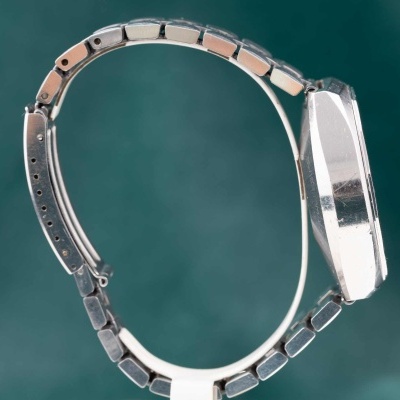 Relógio de pulso metálico prateado de lado com bracelete articulada e fecho ajustável