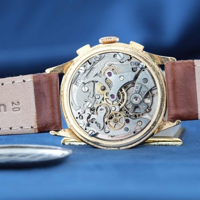 Relógio mecânico dourado com mecanismo interno visível e bracelete castanha de couro