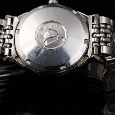 Relógio de pulso metálico prateado visto pelo verso da caixa e bracelete sobre fundo preto