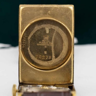 Relógio de pulso com caixa dourada interior com marcações, correia de pele castanha e bege.