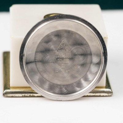 Fundo de caixa de relógio em metal prateado com inscrições gravadas em suporte branco.