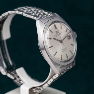 Relógio analógico prateado com mostrador branco e indicação de data