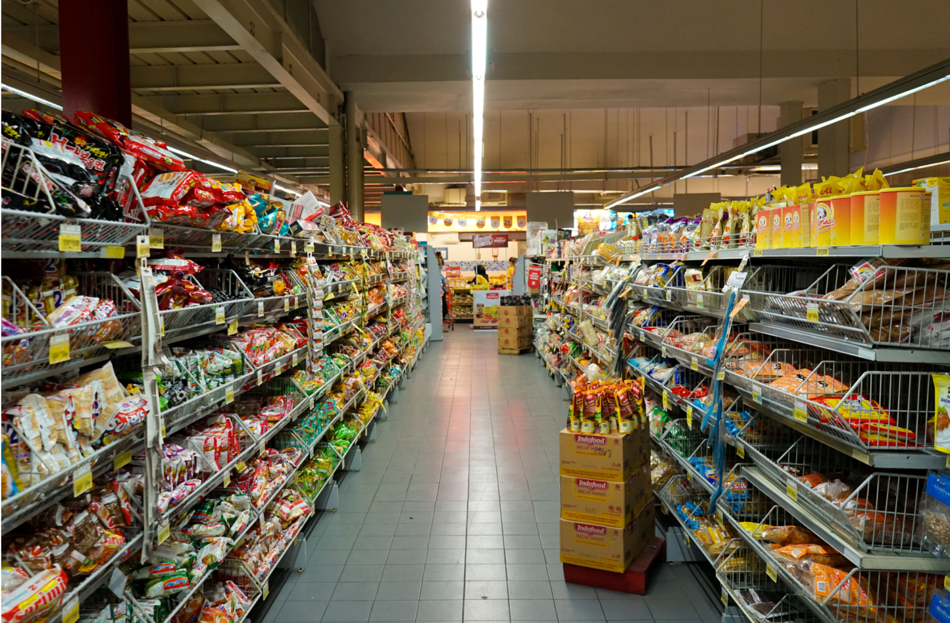 Corredor de supermercado com prateleiras de produtos alimentares e chão cinzento.