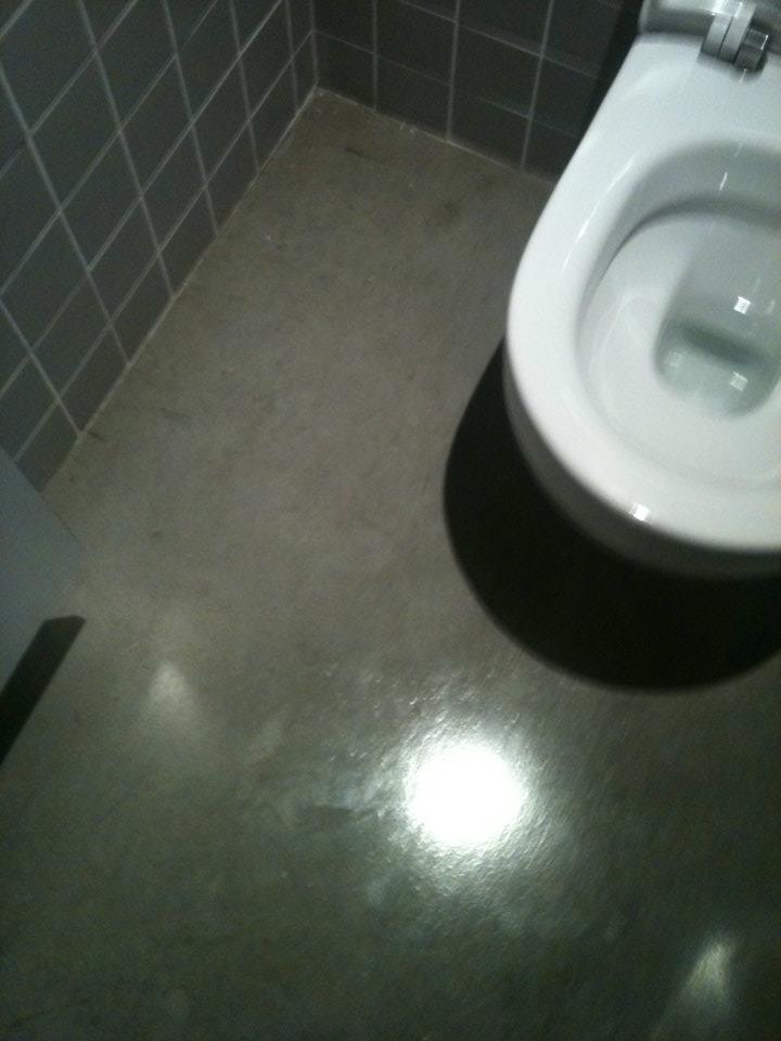 Vaso sanitário branco num chão cinza polido e paredes de azulejos cinzentos