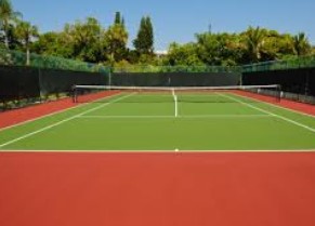 Campo de ténis ao ar livre com piso verde e vermelho cercado por rede preta e árvores ao fundo