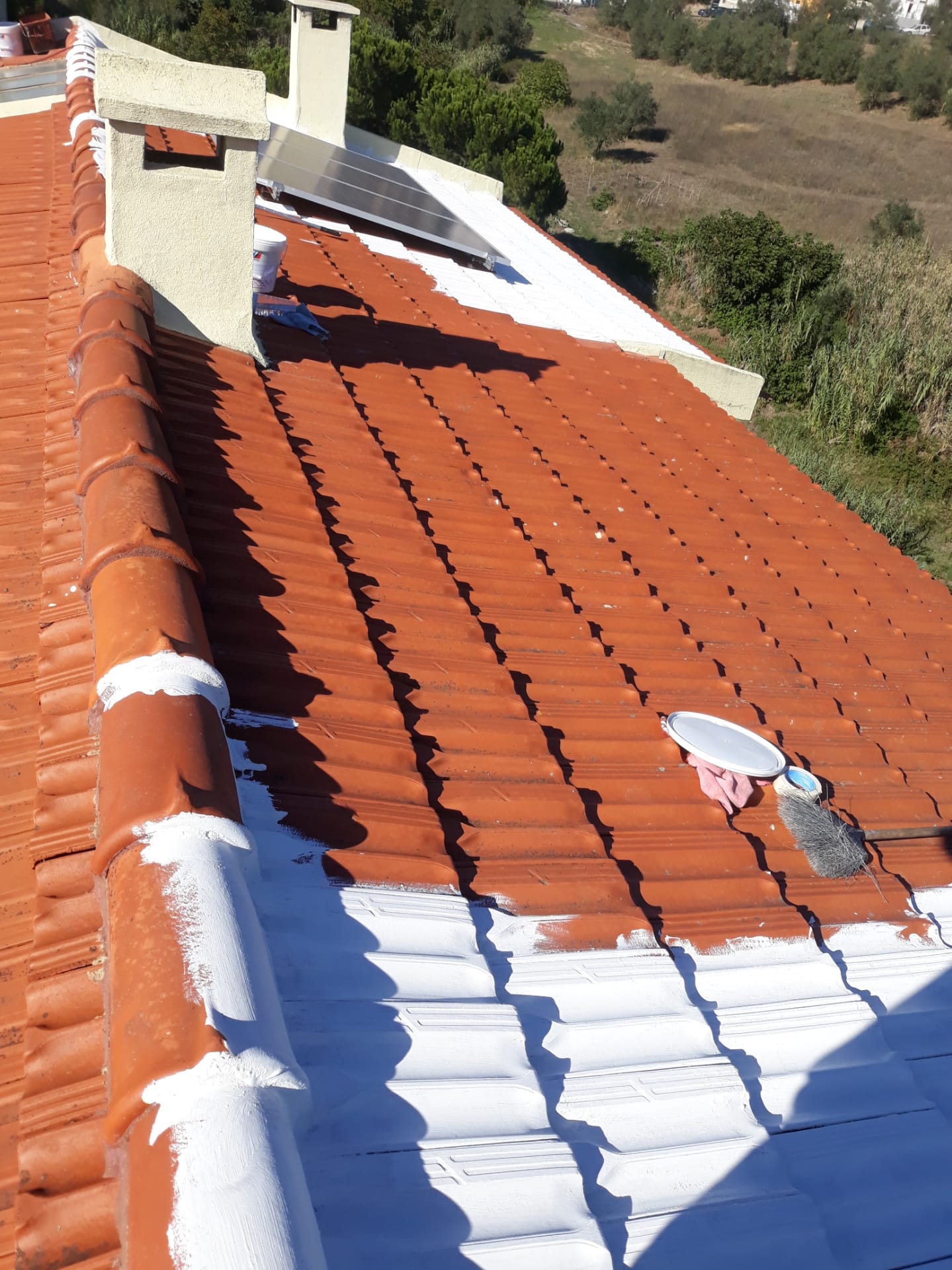 Telhado com telhas cerâmicas vermelhas parcialmente pintadas de branco com pincel e tinta