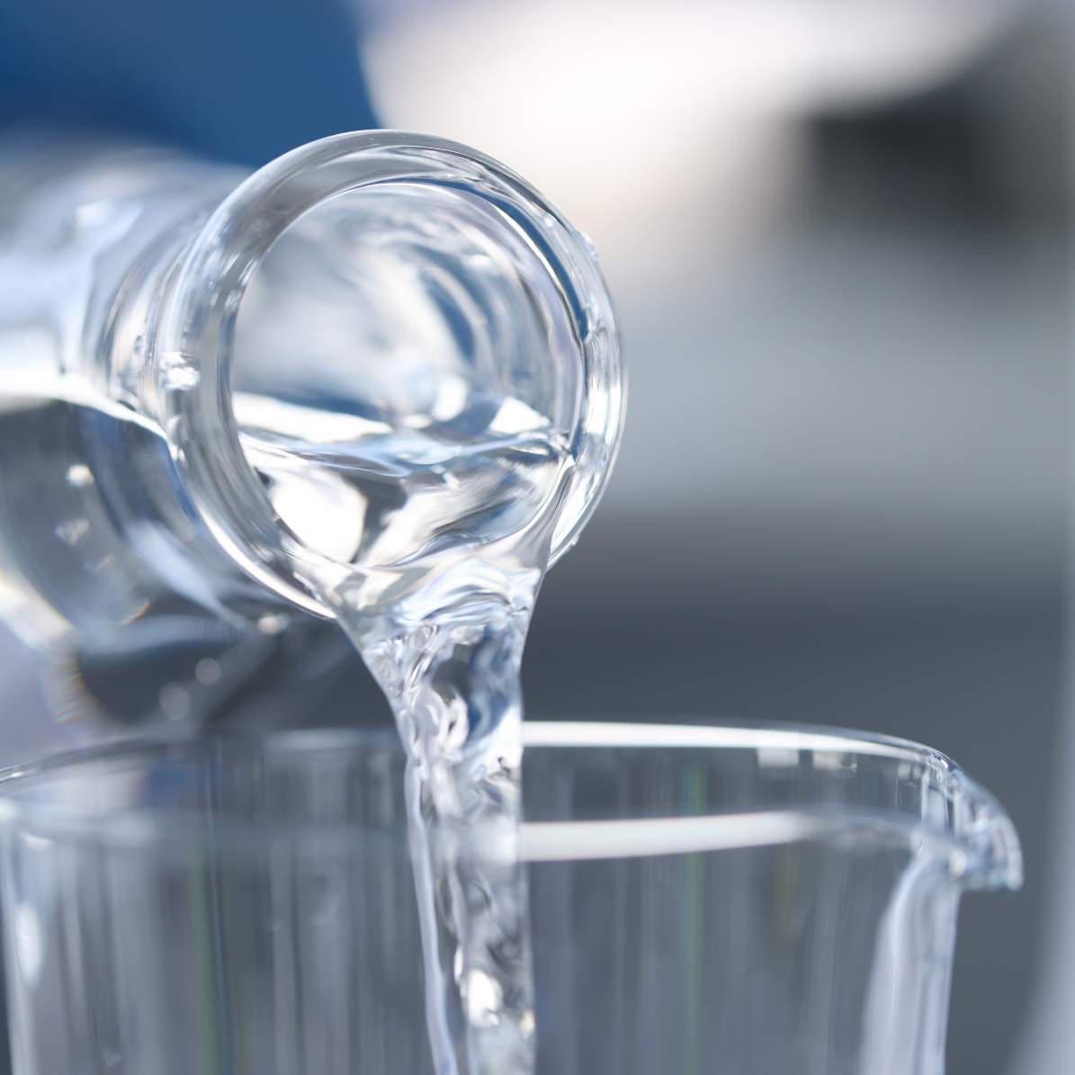 Líquido transparente a ser vertido de garrafa de vidro para recipiente de vidro.