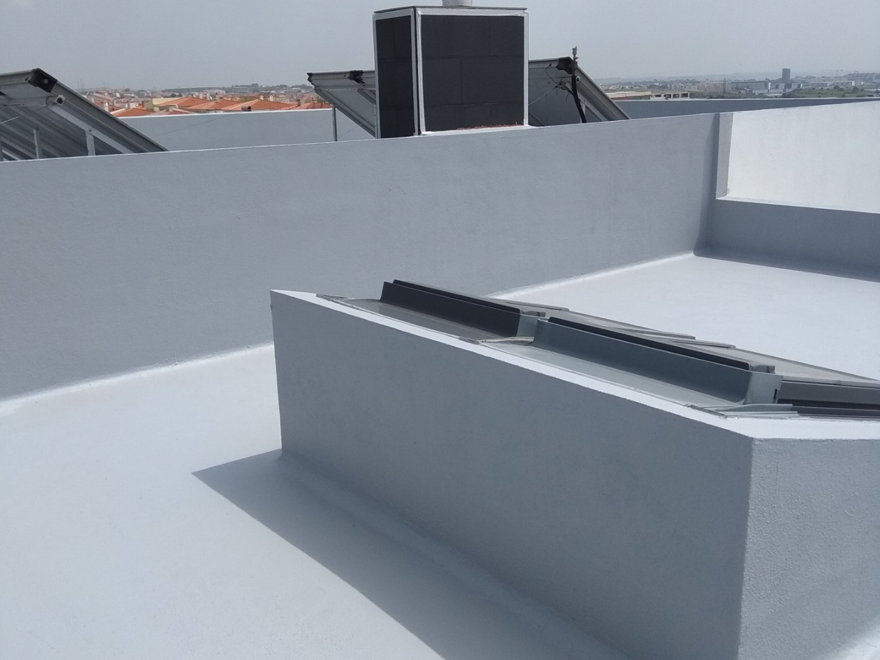 Telhado plano branco com aparelhos solares cinza escuro e vista urbana ao fundo