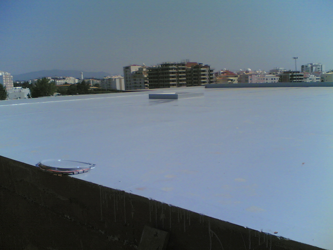 Telhado plano branco com estruturas circulares e edifícios ao fundo